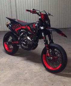 a red and black dirt bike parked in front of a garage door on cement floor