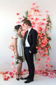 a man and woman standing next to each other in front of a wall covered with balls