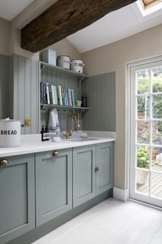 a kitchen with blue cabinets and white counter tops, bookshelf above the sink