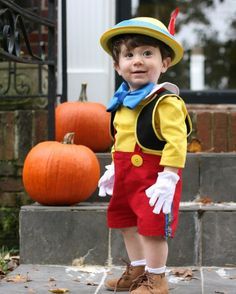 a young boy dressed up in mickey mouse costume and hat, standing on steps with pumpkins behind him