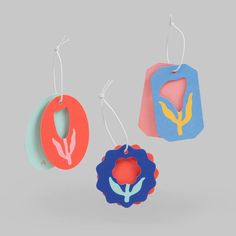 three colorful tags hanging from hooks on a gray background, each with an ornament shaped like a flower