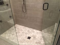 a walk in shower sitting next to a glass door and tiled floored area with hexagonal tiles on the walls