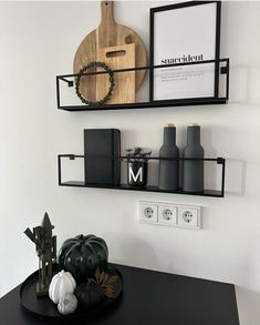 two black shelves on the wall above a table with various items and decorations in front of them