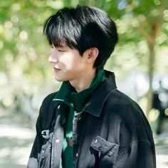 a young man with black hair and green shirt standing on the sidewalk in front of trees