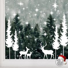 the window is decorated with white silhouettes of deer and trees in snowflakes