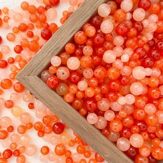 some red and orange beads are in a wooden box on a white surface with a wood frame