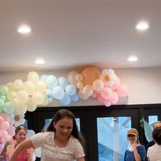 a group of people standing in front of a table with cake and balloons on it