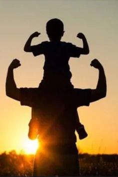 the silhouette of a man holding a child in his arms as the sun sets behind him