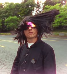 a man with long hair and sunglasses on standing in the middle of a parking lot