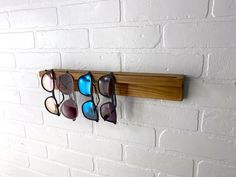 several pairs of sunglasses are hanging on a wooden rack against a white brick wall with eyeglasses in them