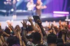 a group of people raising their hands in the air at a music concert with one person on stage