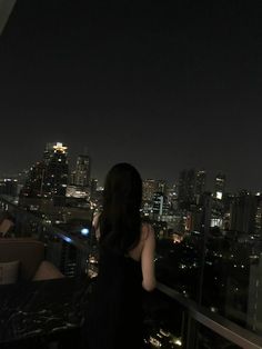 a woman standing on top of a roof looking at the city lights in the distance