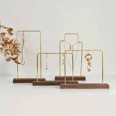 three gold jewelry stands with necklaces and earrings on them, one is holding a plant