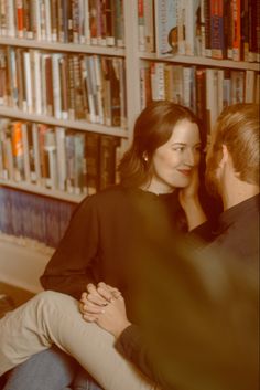 a man and woman sitting in front of a bookshelf with their arms around each other