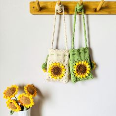 two crocheted sunflower purses hanging on a wall next to a vase with flowers