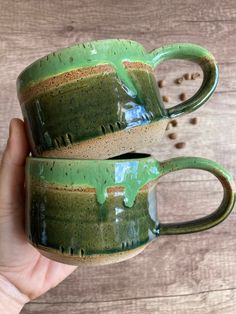 two green coffee mugs sitting next to each other on top of a wooden table