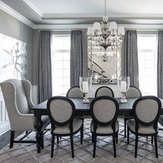 a dining room table with chairs and chandelier in front of two windows that have drapes on them