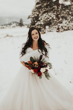 a woman standing in the snow wearing a wedding dress and holding a bridal bouquet