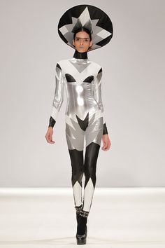 a woman in a futuristic suit and hat walks down the runway