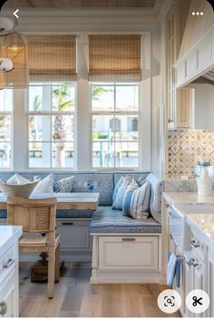 a kitchen with white cabinets and blue cushions on the bench in front of the window