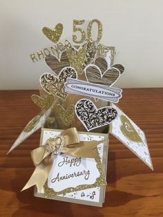 a 50th anniversary card in a vase with gold ribbon and heart cutouts on it