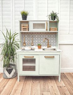 an old fashioned kitchen with plants on the counter and sink in front of white walls