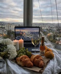 an open laptop computer sitting on top of a table next to bread and wine glasses