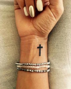 a woman's wrist with a cross tattoo on it and two different bracelets