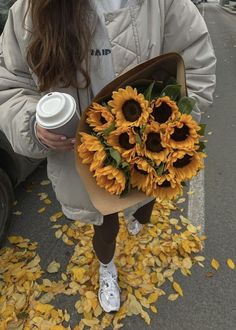 a woman holding a bouquet of sunflowers and a cup of coffee in her hands