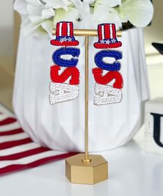 two red, white and blue beaded earrings on a gold stand with flowers in the background