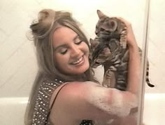 a woman holding a cat up to her face in the bathtub with water on it