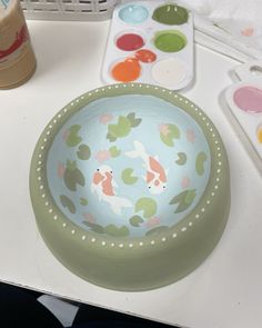 there is a bowl with fish on it and some paint next to it, along with other items