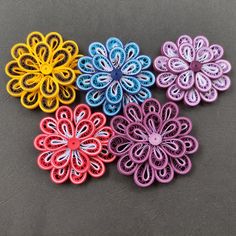 four different colored paper flowers sitting on top of a gray surface with one flower in the middle