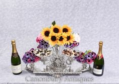 two bottles of champagne and three sunflowers on a silver tray with cupcakes