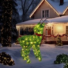 a lighted deer in front of a house with christmas lights on it's roof