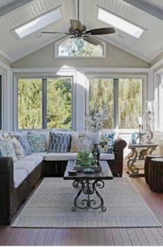 a living room filled with lots of furniture under a ceiling fan and two windows above the couches