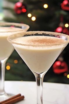 two martini glasses filled with white wine and cinnamon on a table in front of a christmas tree