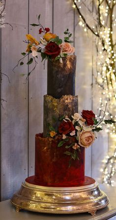 a three tiered cake decorated with flowers and greenery on a gold plated stand