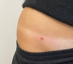 a woman's stomach with a small red heart tattoo on her left side belly