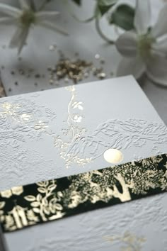 a white and gold wedding card sitting on top of a table next to some flowers