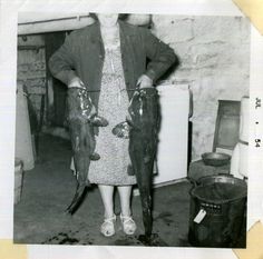 an old black and white photo shows a woman holding two fish in her hands while standing next to a refrigerator