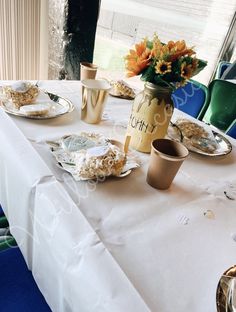 the table is set with plates, cups and vases filled with flowers on it