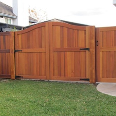 a wooden fence in front of a house next to a green yard with grass and bushes