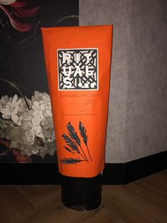 a tube of orange hand cream sitting on top of a wooden floor next to a painting