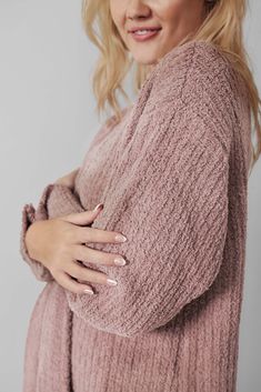 a woman wearing a pink sweater with her arms folded over her chest and looking at the camera