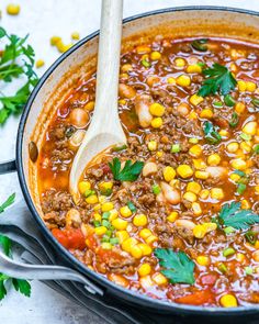 a pot full of chili and corn soup with a wooden spoon