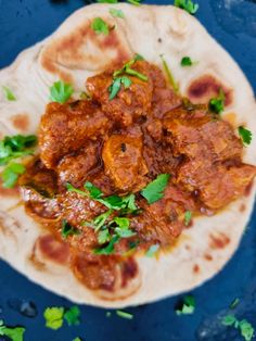 a tortilla topped with meat and cilantro on top of a blue surface