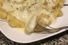 a white plate topped with food covered in sauce and gravy next to a fork