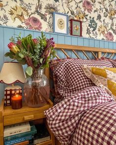 a bed with plaid sheets and pillows next to a night stand with flowers in a vase on it