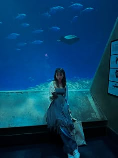 a woman sitting in front of an aquarium looking at her cell phone